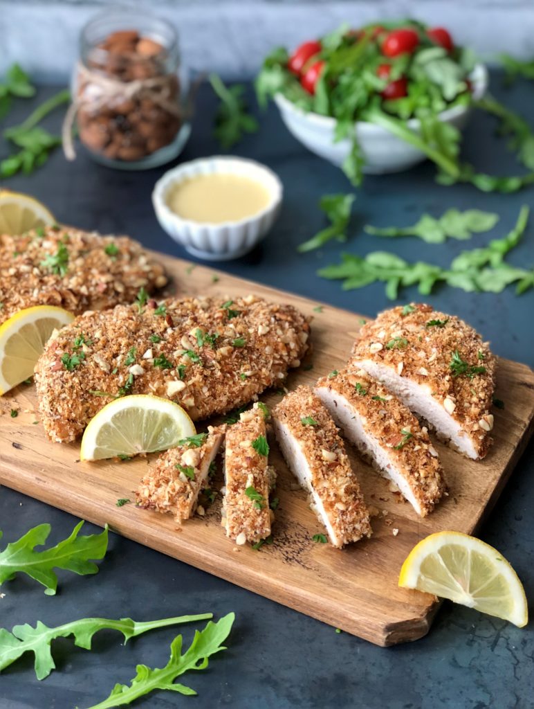 Almond crusted chicken arranged on a wood board with salad.

