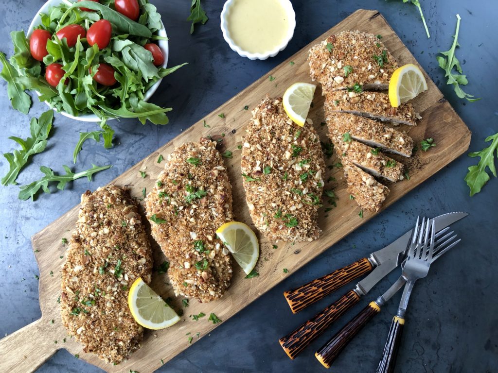 Top down view of almond chicken pieces on a wood board with salad and dip.