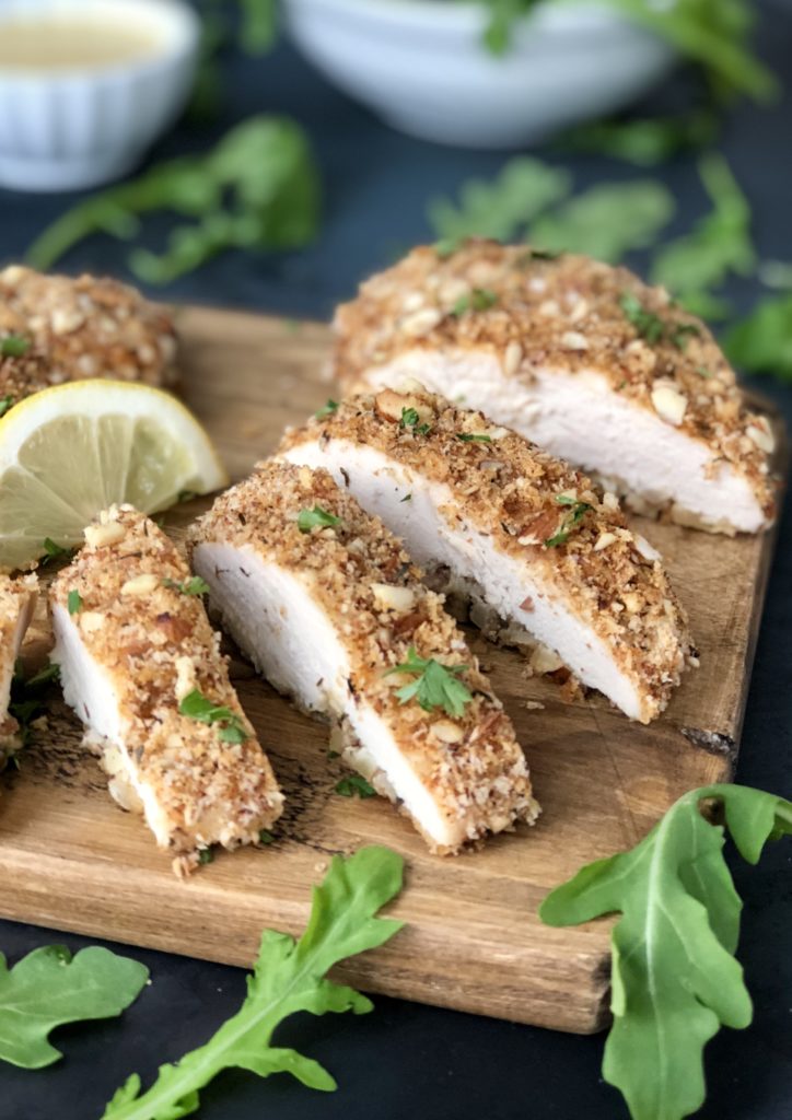 Piece of almond crusted chicken sliced on a wood board.
