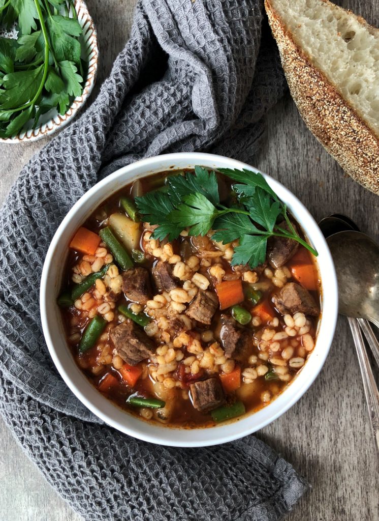 Single bowl of hot soup with spoons and crusty bread.