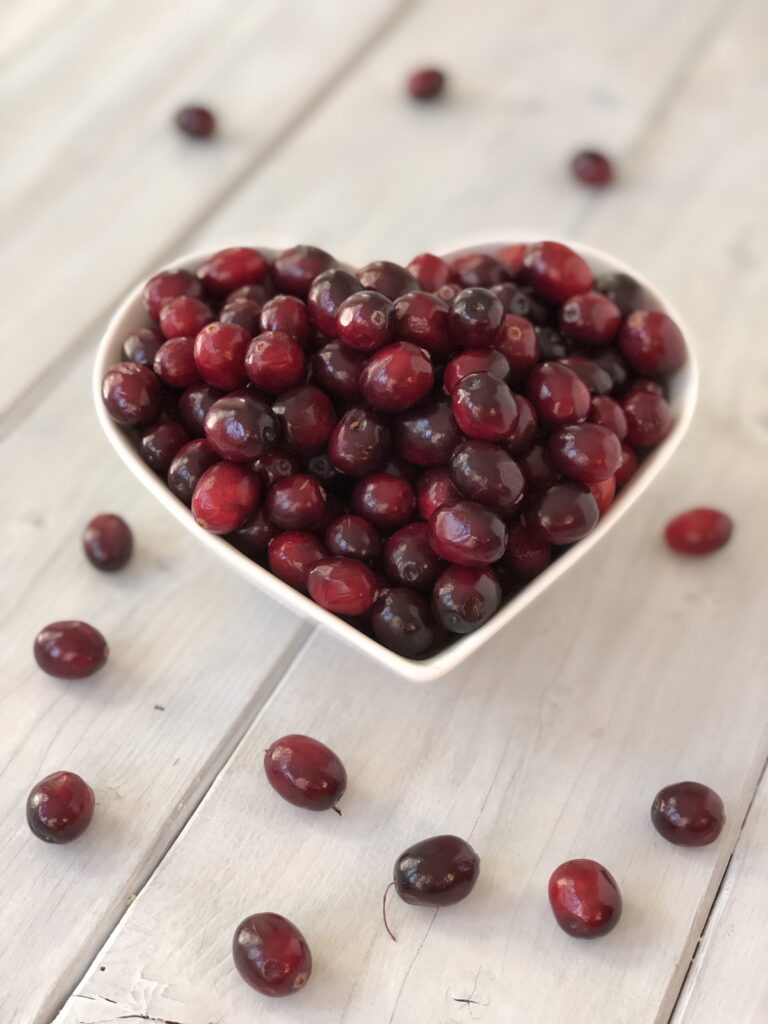 White heart shaped bowl filled with fresh cranberries.
