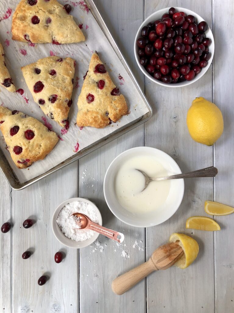 Scones on parchment paper being glazed with a spoon of icing.