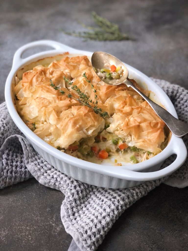 Hot phyllo chicken pot pie casserole on tea towel with serving spoon.