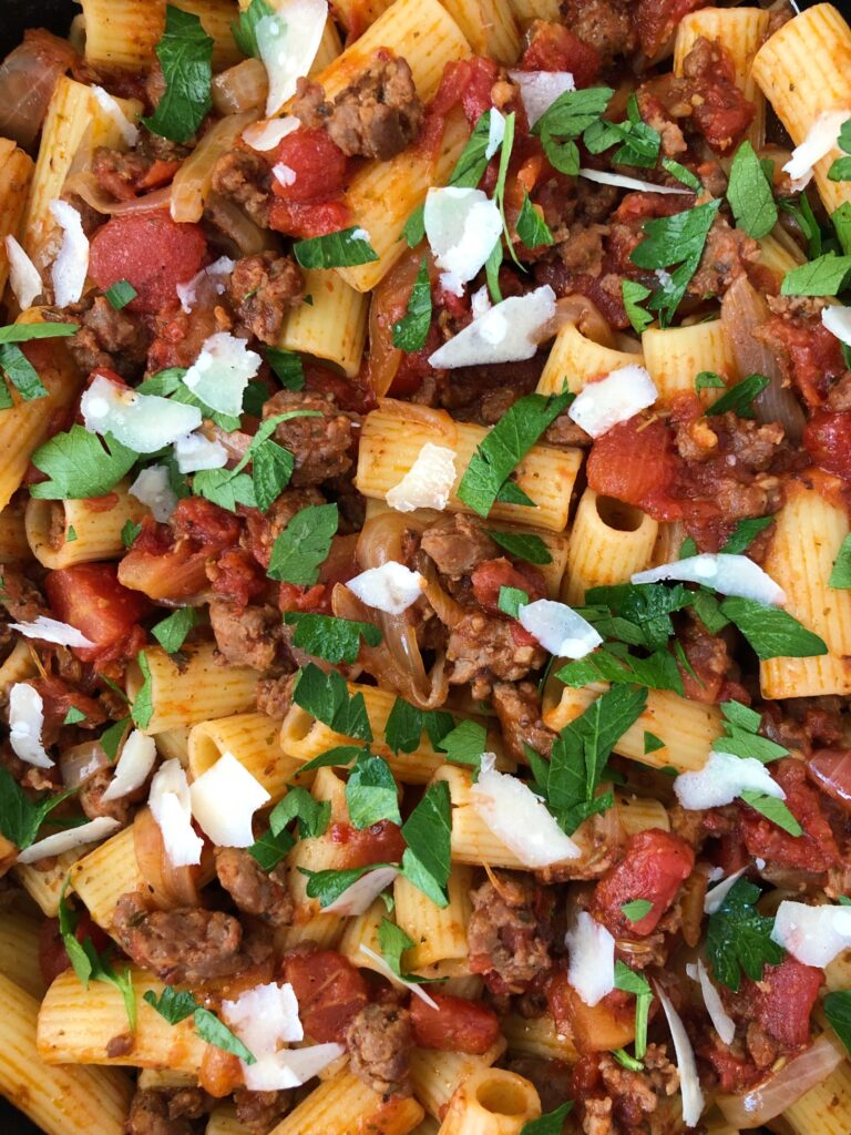 Zoomed in closeup view of italian sausage pasta garnished with parmesan and parsley.