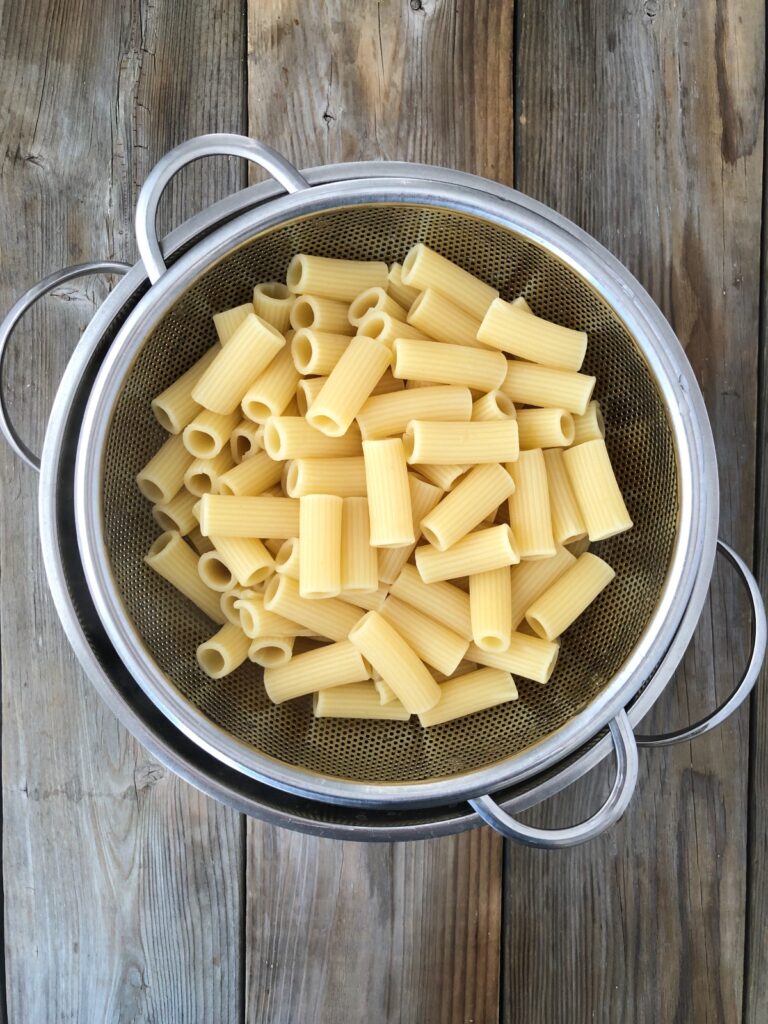 Cooked rigatoni draining in a stainless steel colander