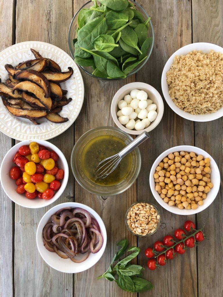 Ingredients ready for assembling bowls, mushrooms, spinach, tomatoes, onions, chickpeas, cheese, dressing.