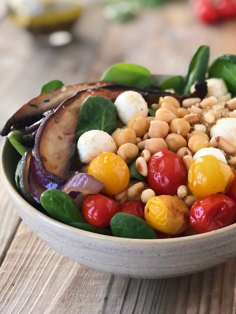 Mushroom bowl filled with mushrooms, quinoa, spinach, tomatoes, chickpeas, cheese balls and pine nuts.
