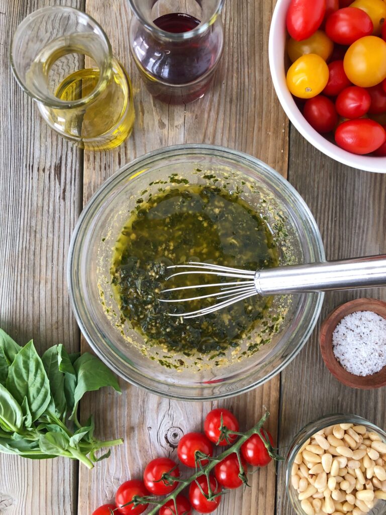 Pesto, olive oil, vinegar, salt and pepper whisked in a bowl.