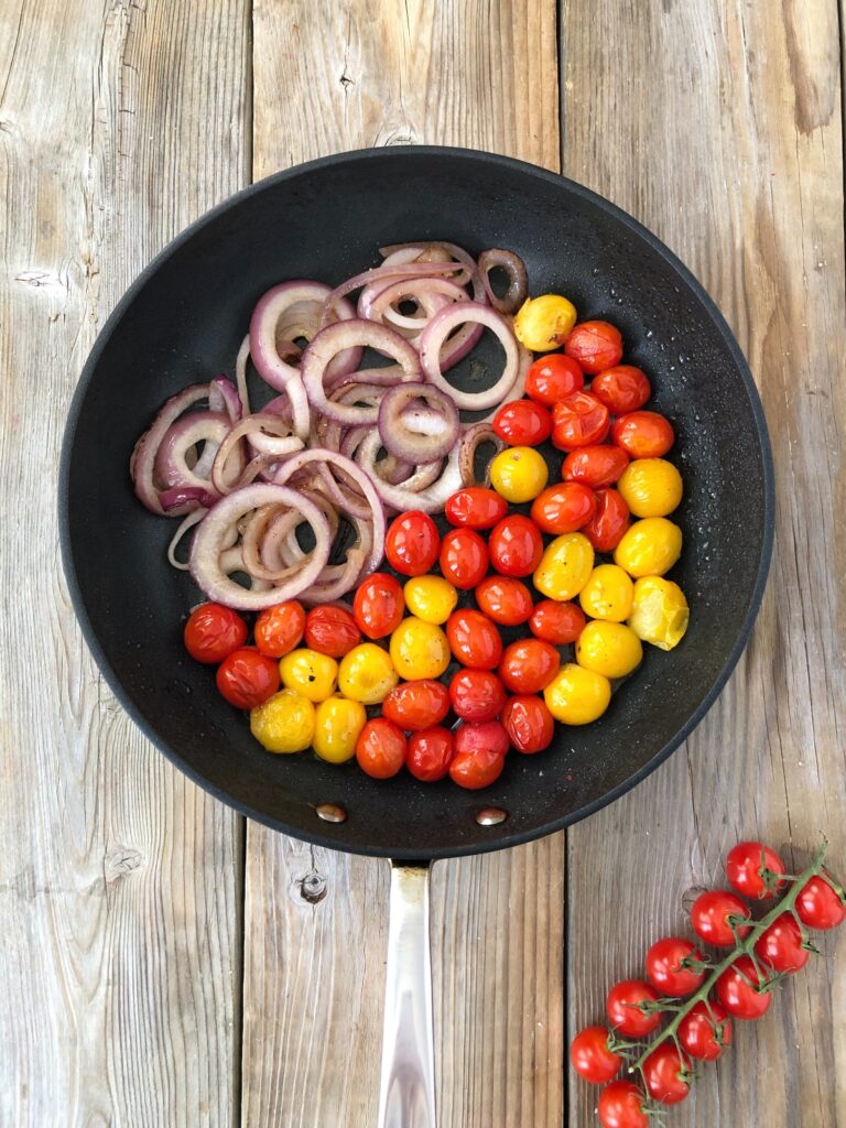 Onions and tomatoes sautéed in a skillet.