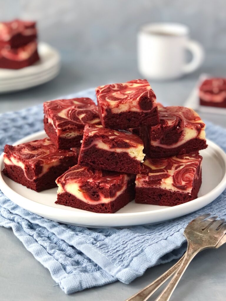 Cream cheese brownies piled on a plate ready to serve with forks.