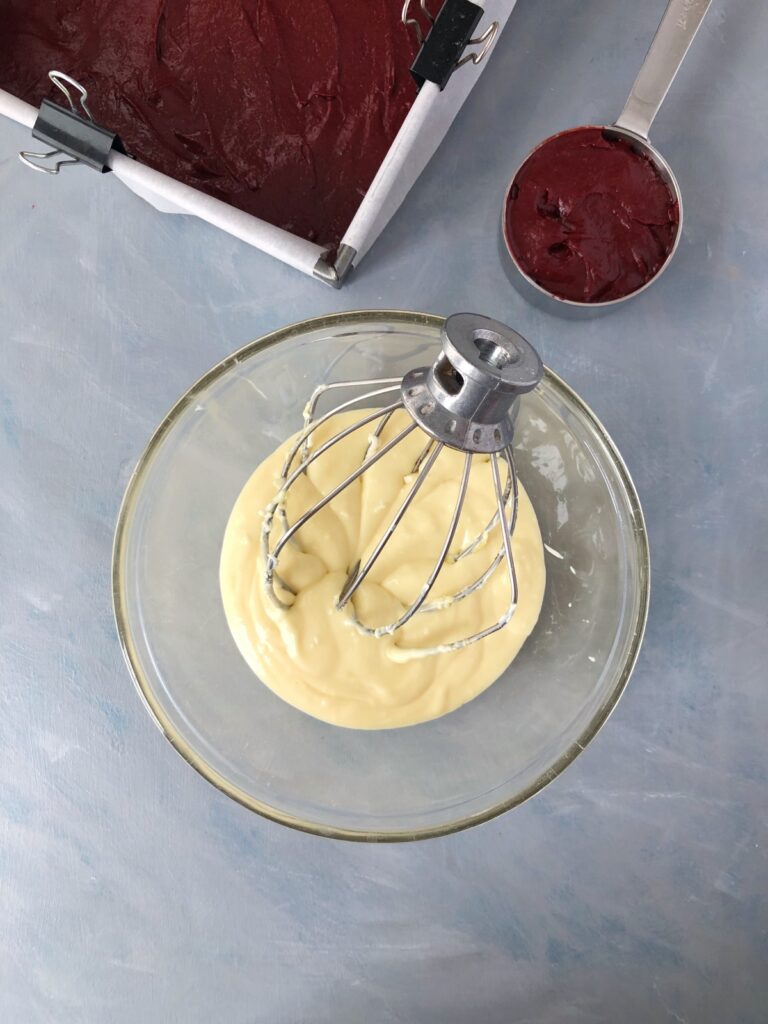 Cheesecake batter mixed in a clear bowl with a whisk.
