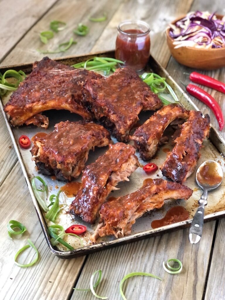 Juicy oven baked pork ribs on a tray slathered in sauce ready to serve