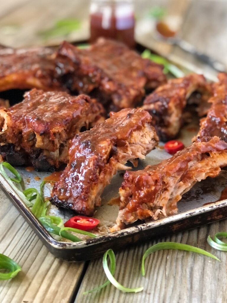 Close view of succulent cooked ribs with BBQ sauce on a tray.