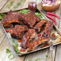 Saucy and sticky pork ribs sliced on a tray with barbecue sauce.