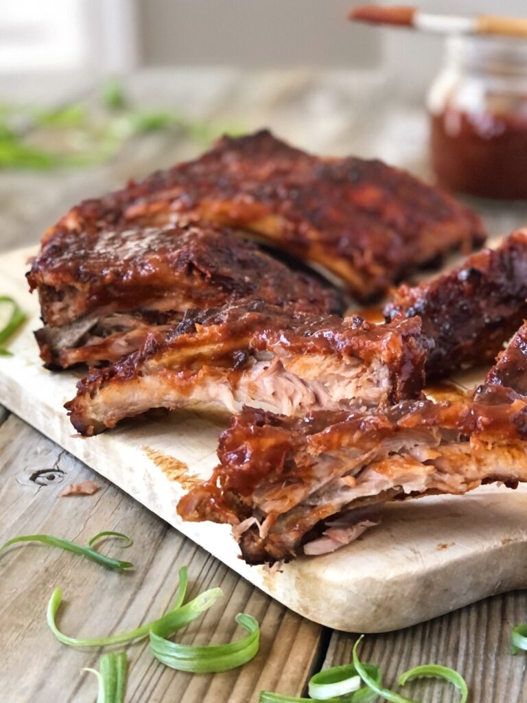 Fall of the bone tender oven baked ribs on a board covered in barbecue sauce