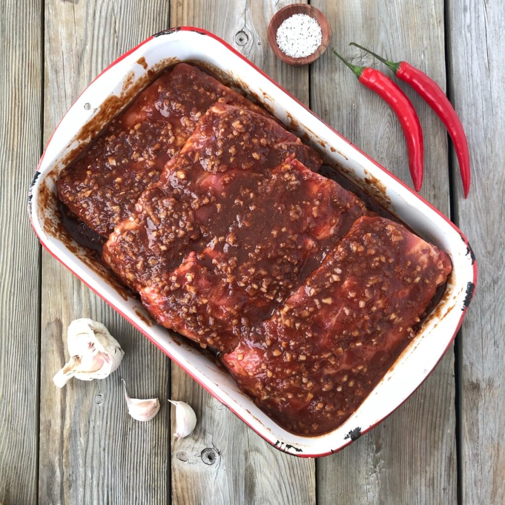 Uncooked ribs covered in barbecue sauce in a pan ready for oven.