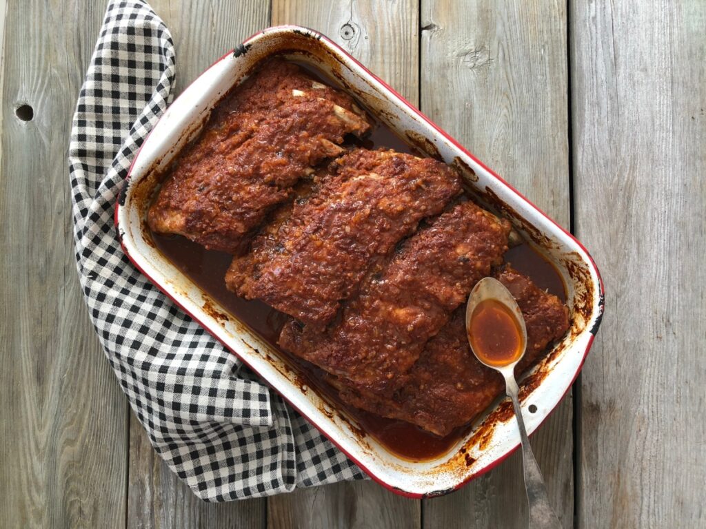 Partially cooked ribs being basted with sauce drippings