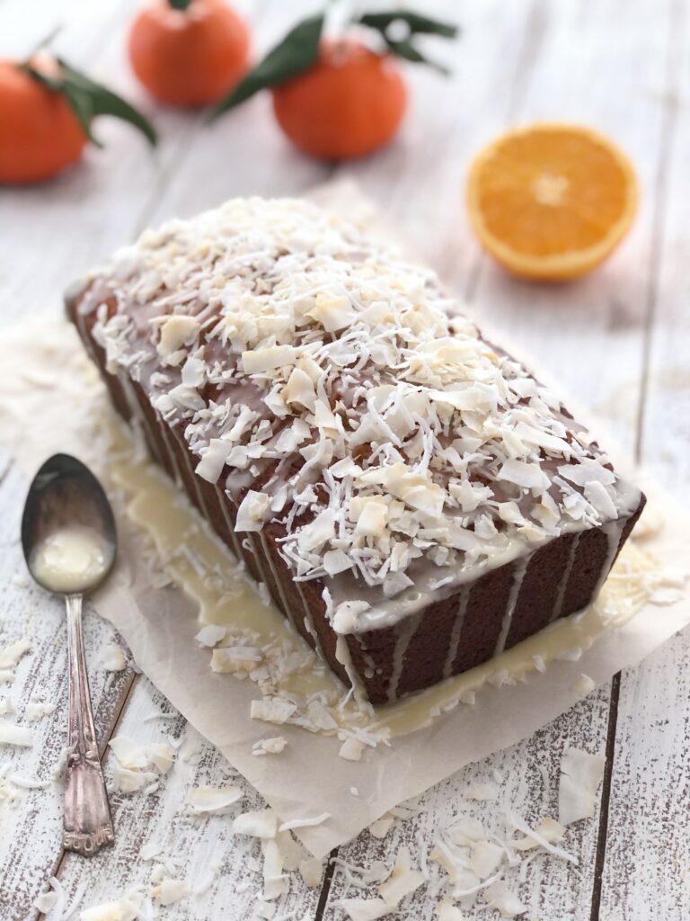 Baked coconut loaf on parchment paper drizzled with glaze and coconut sprinkles.