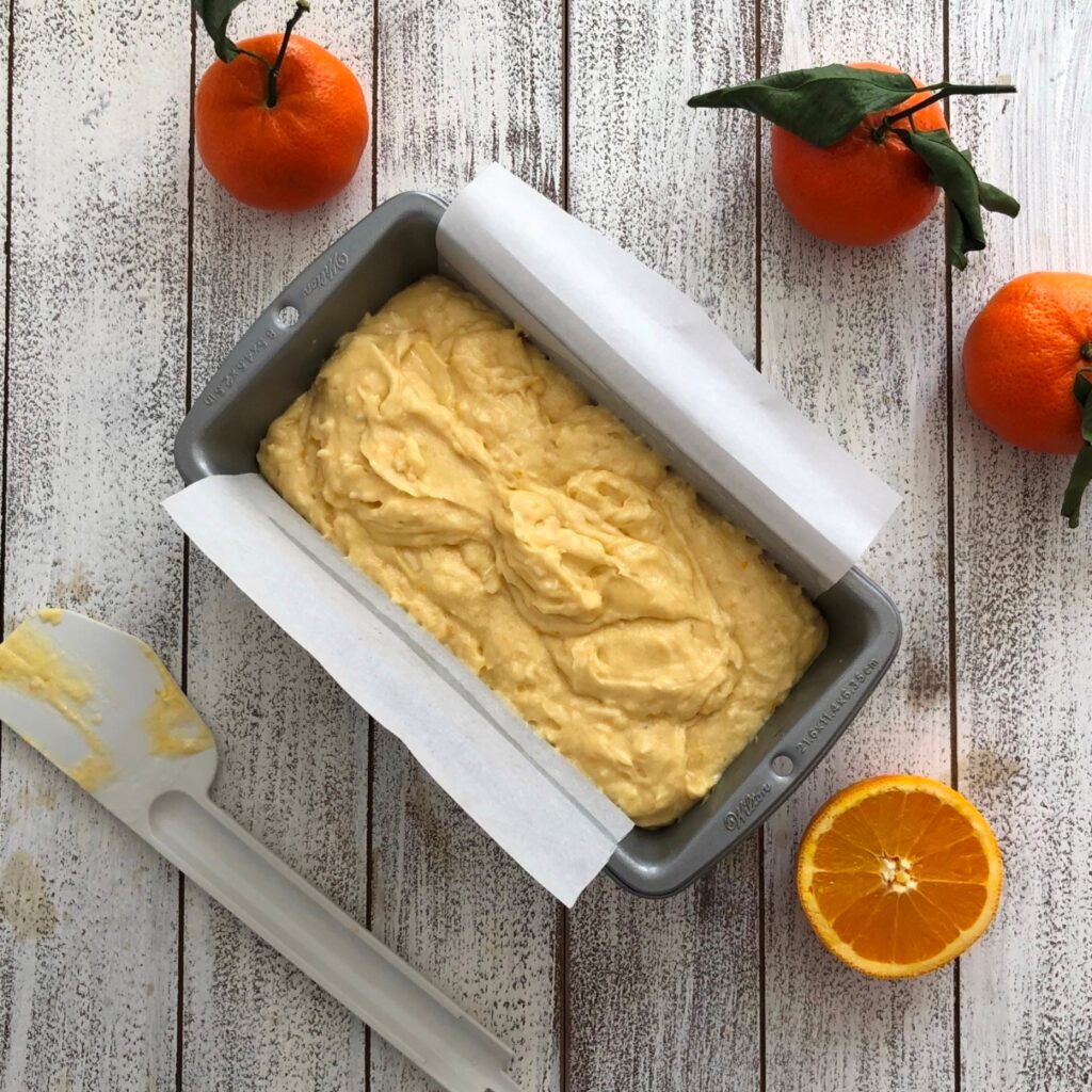 Orange coconut cake batter spread in a loaf ban ready to bake.