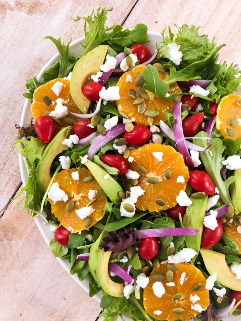 Top down view of mixed greens salad garnished with oranges and goat cheese.