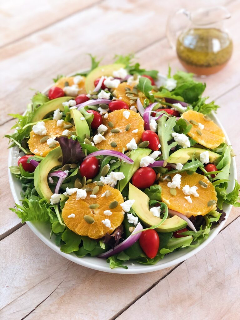 Refreshing orange salad with mixed greens and goat cheese assembled on a platter.