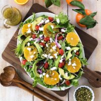 Mixed greens orange salad with goat cheese ready to serve on a board.