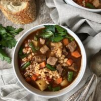 Full bowl of beef barley soup with parsley garnish.