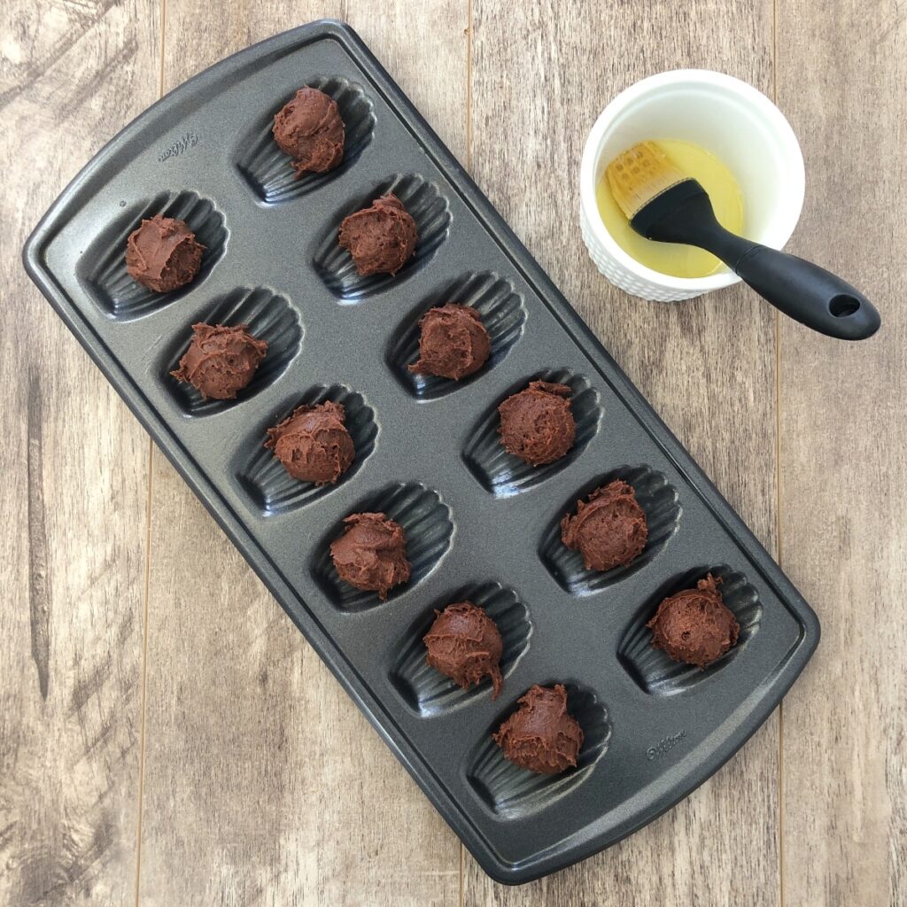 Chocolate batter dolloped into Madeleine pan cavities.