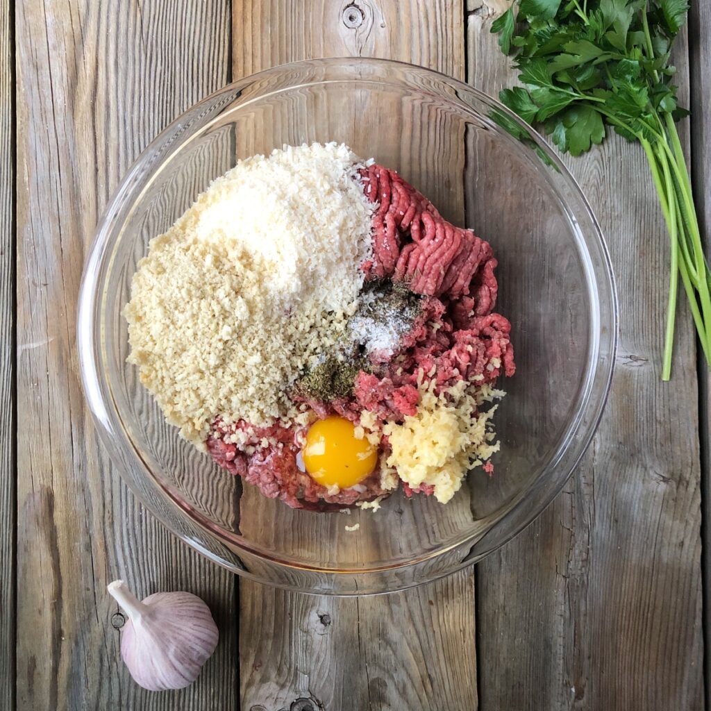 Meatball ingredients added to a glass bowl.