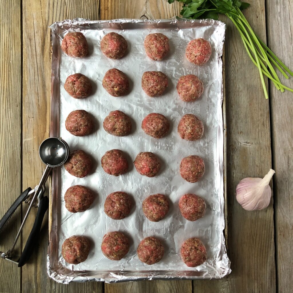 Formed beef meatballs on a baking sheet.