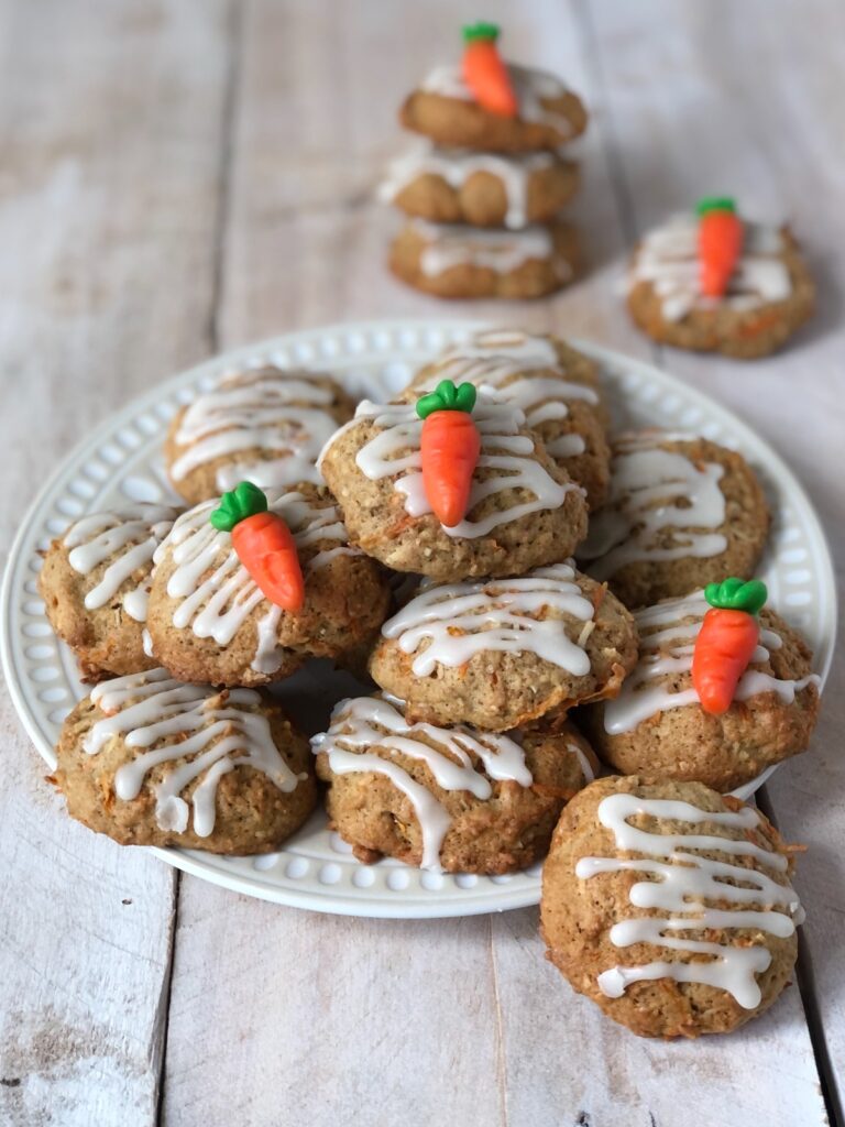 Carrot cake cookies piled on a white plate with carrot gummy garnish.