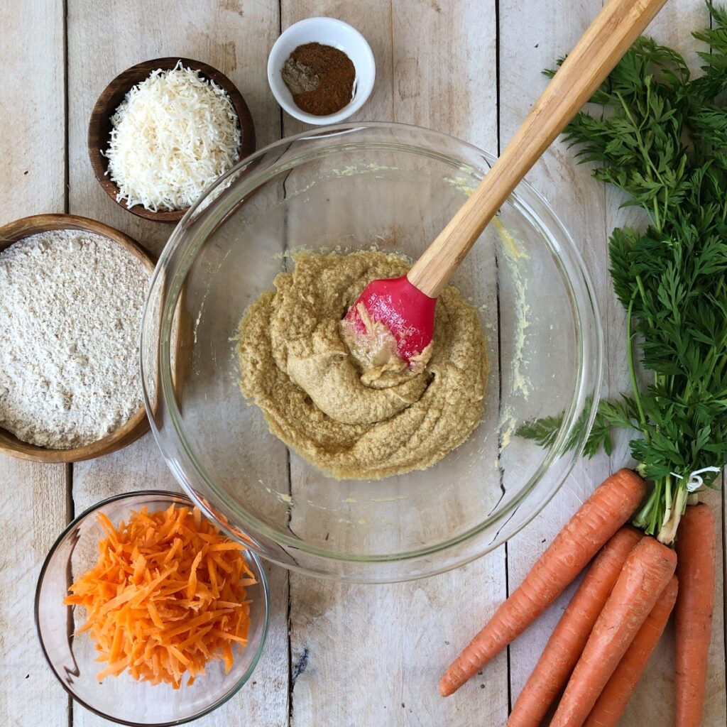 Carrot and eggs mixed in a mixing bowl with spatula.