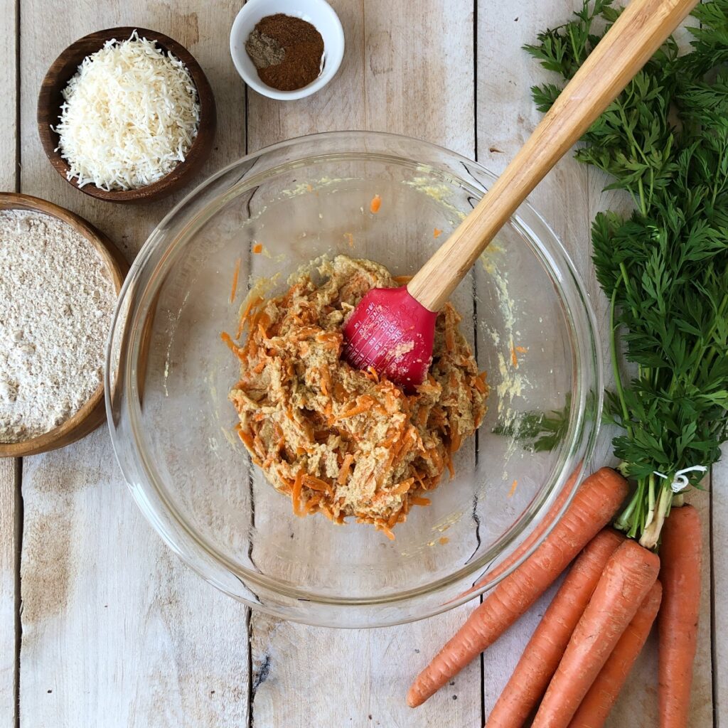 Shredded carrots added to batter in mixing bowl.