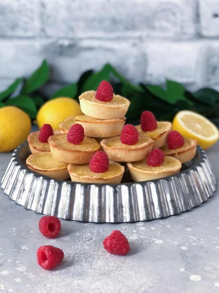 Lemon tarts with raspberries piled on a metal tart pan.