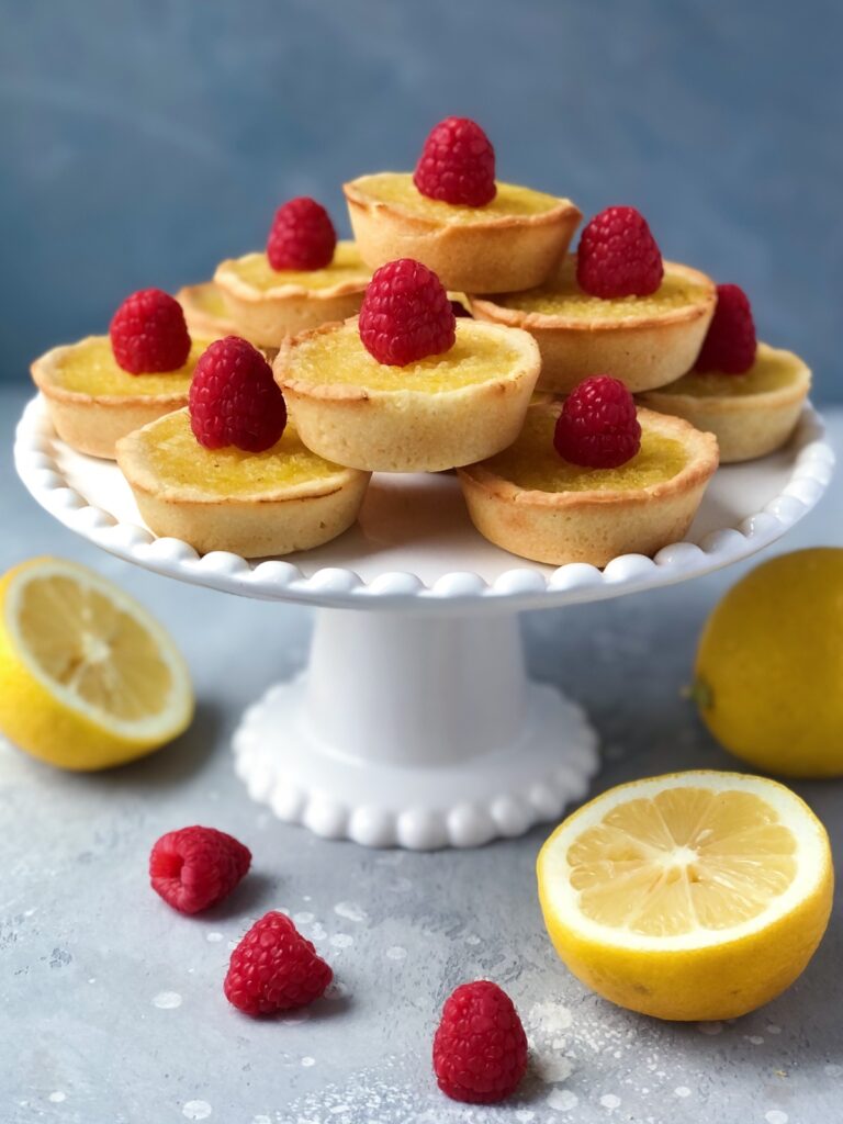 Lemon tarts arranged on a white pedestal platter.
