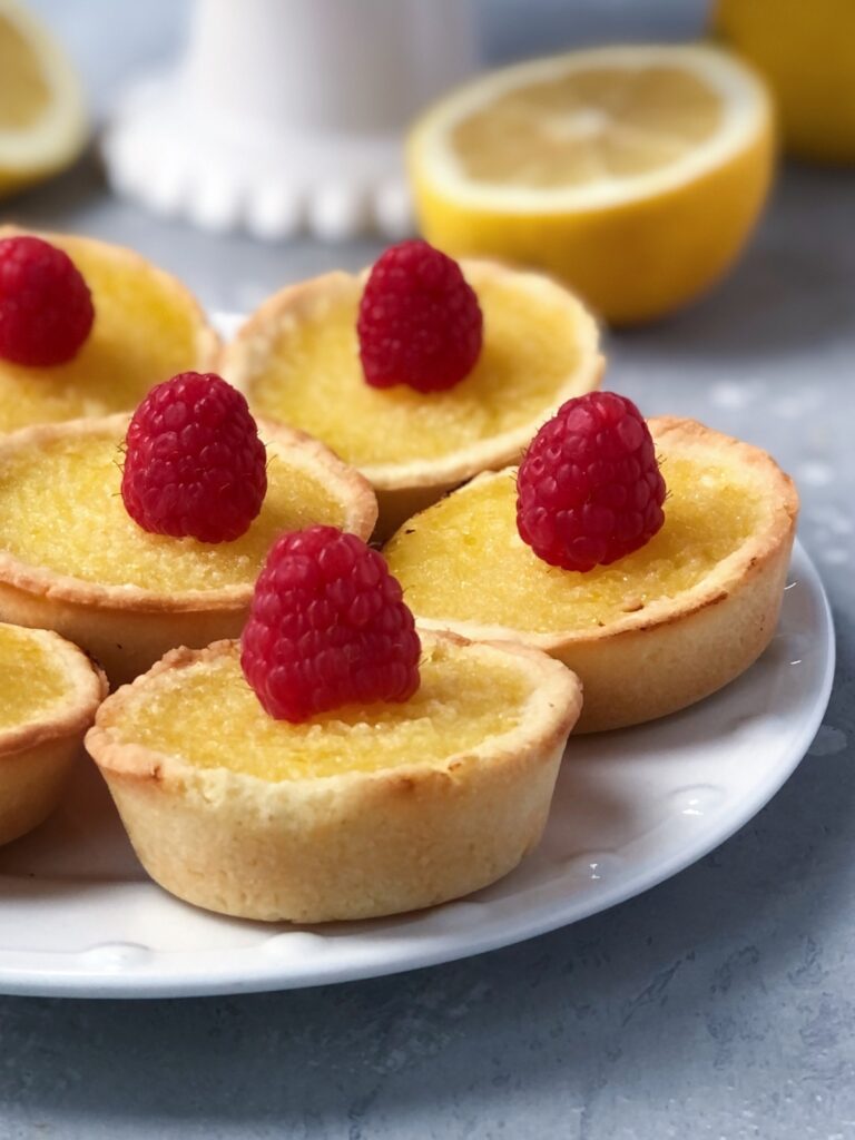 Close view of lemon tarts topped with raspberries on a plate.
