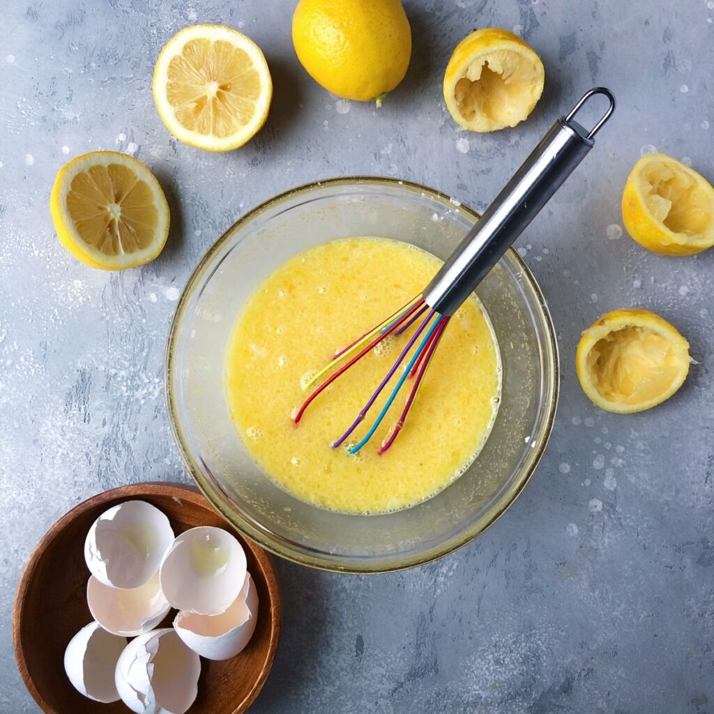 Eggs whisked into lemon sugar mixture to create a curd.