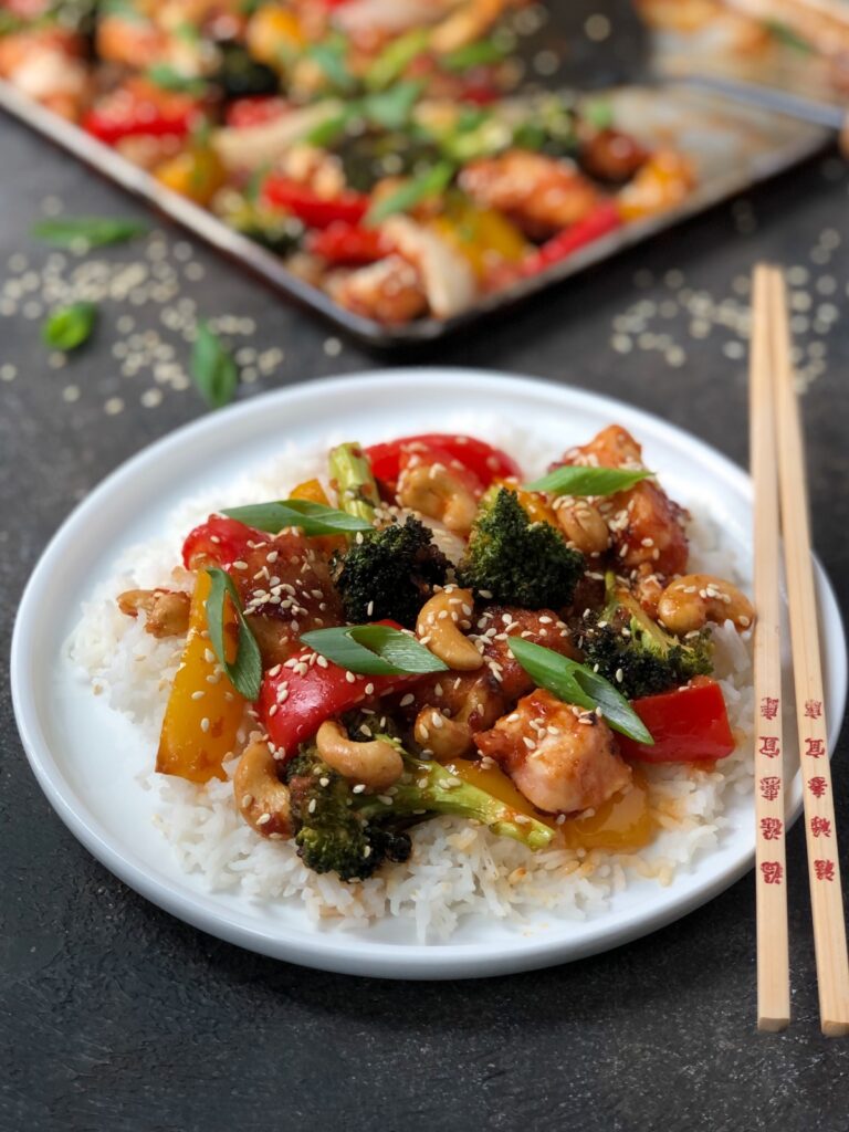 Plate with chicken and vegetables over rice with chopsticks beside.