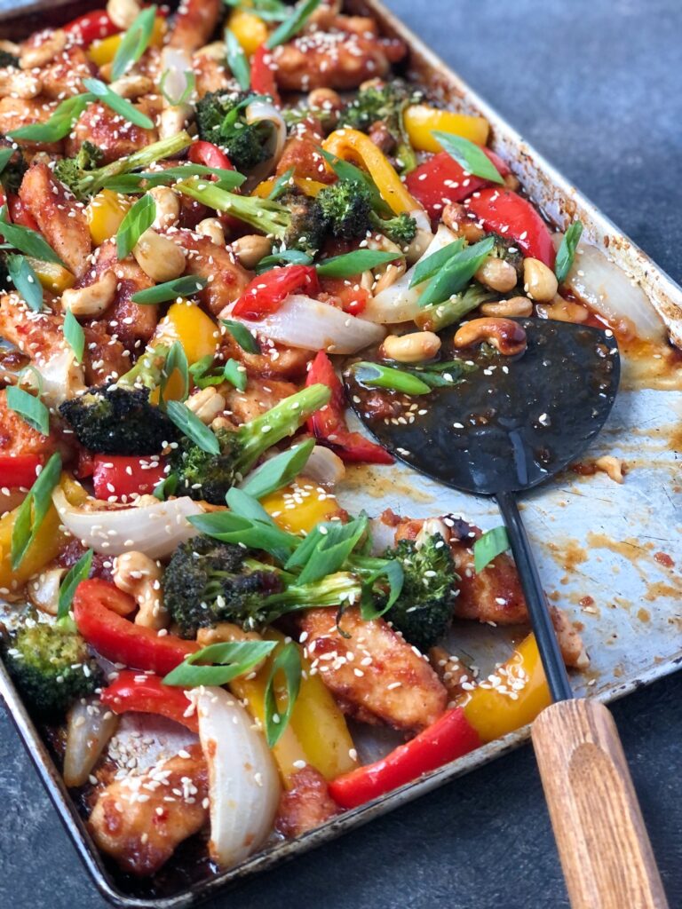 Flat scoop on sheet pan dishing out cooked chicken, cashews and vegetables.