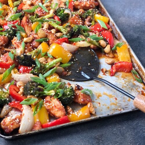 Square image of vegetables, chicken and cashews being served with a scoop.