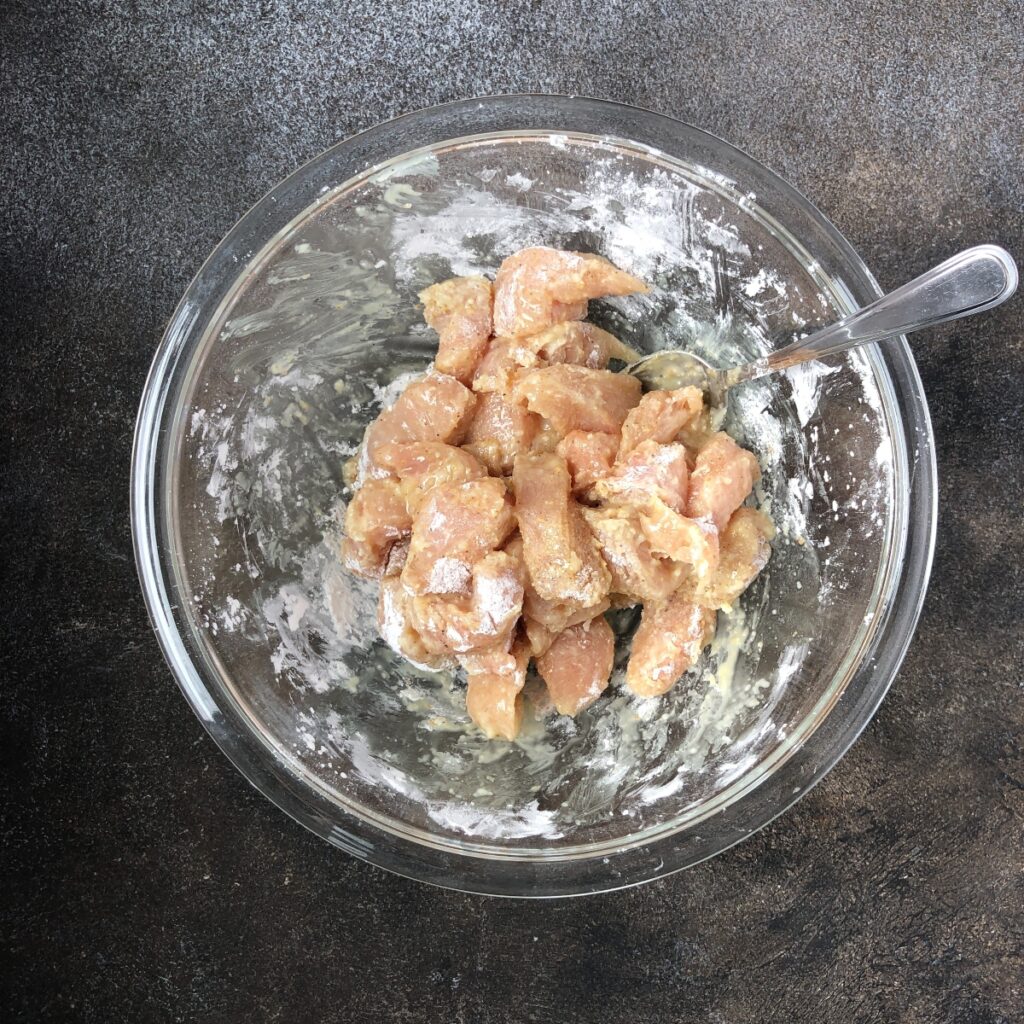 Chicken in a glass bowl seasoned and coated in cornstarch.