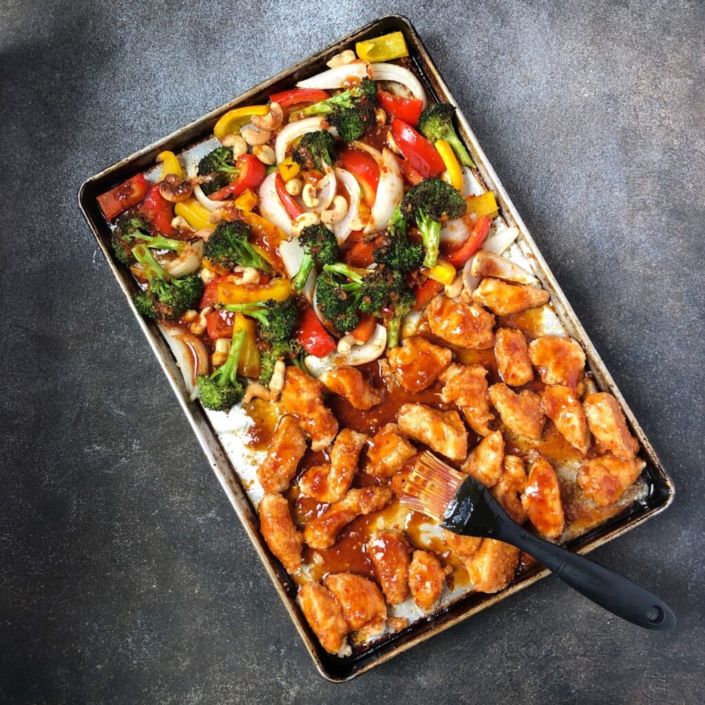 Partially baked chicken and vegetables being brushed with sauce.