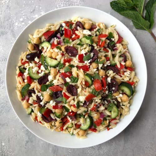 Square image of Greek orzo pasta salad in a serving bowl.